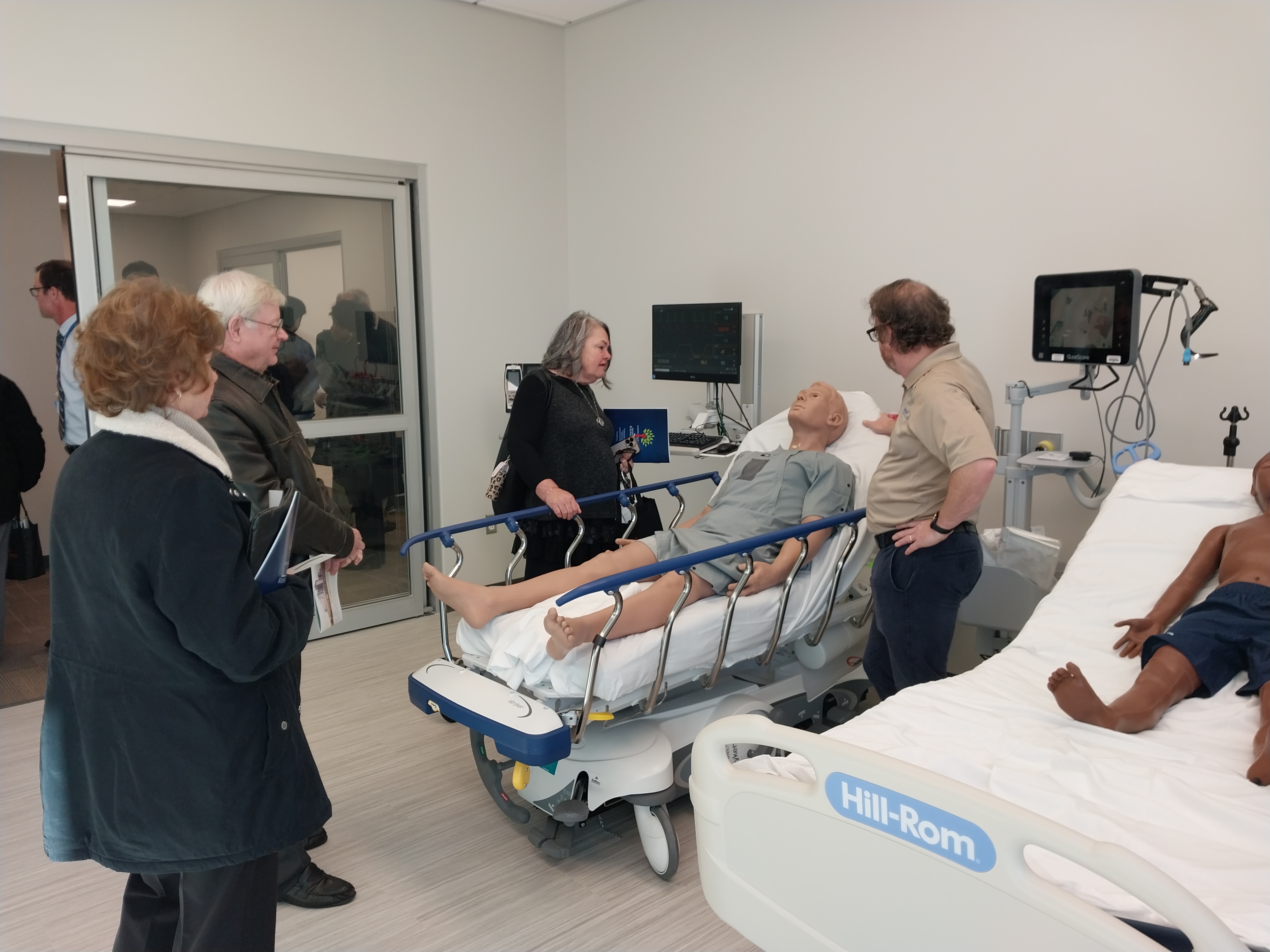 Guests receiving a tour of the new facility interact with the AI patient “John” who will be used by medical residents to simulate real patient needs. Photo provided by: GFBJ