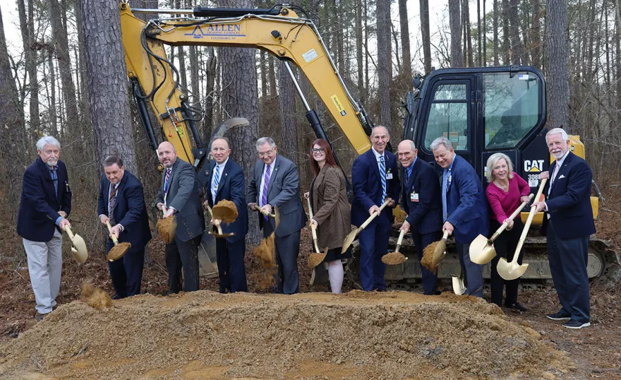 A group of people with shovels standing in front of a piece of construction equipment.