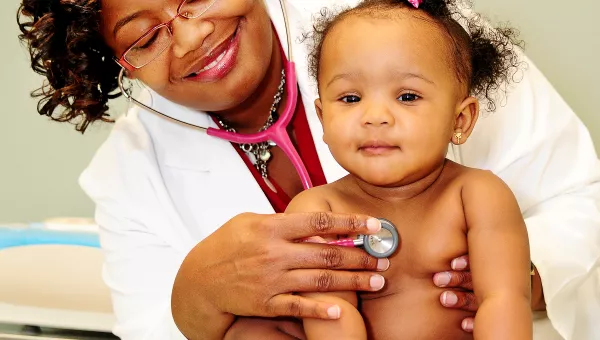 Pediatrician smiling at a baby with a stethoscope while baby smiles back 