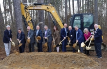 A group of people with shovels standing in front of a piece of construction equipment.